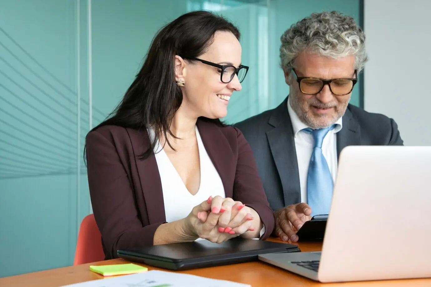 Жизнерадостные коллеги или деловые партнёры встречаются и обсуждают проект, сидят за открытым ноутбуком, используют планшет, разговаривают и улыбаются.